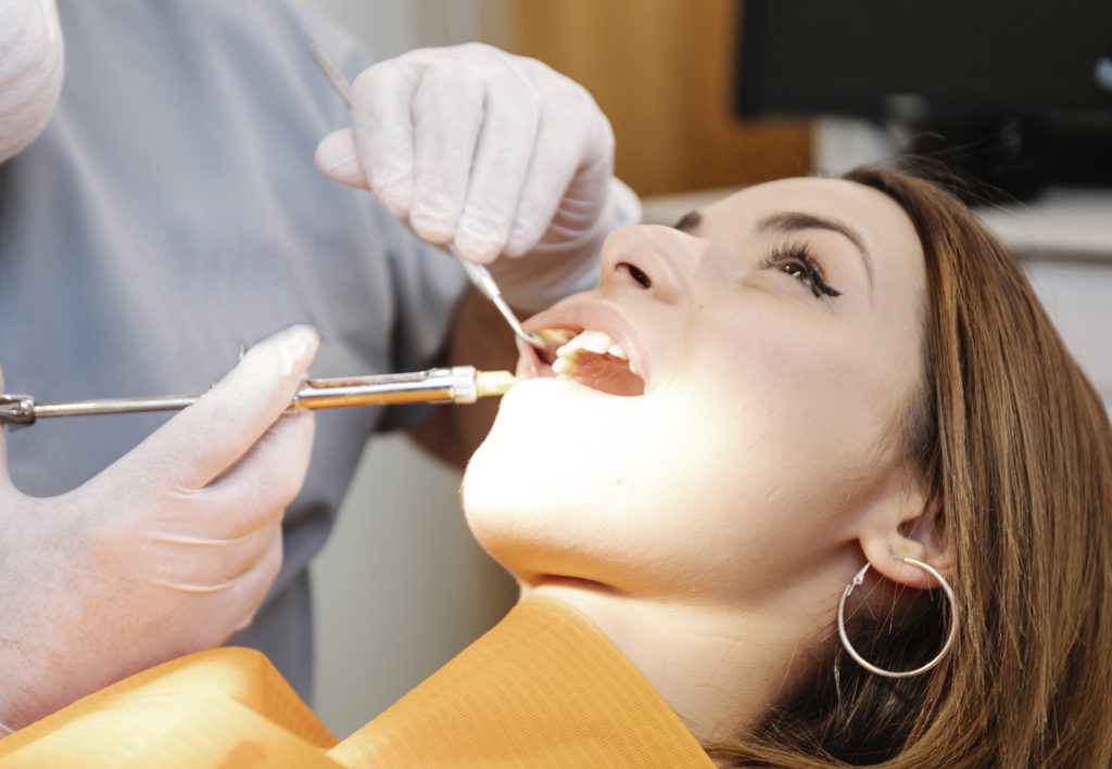 Crop dentist injecting anesthetic into patient gums